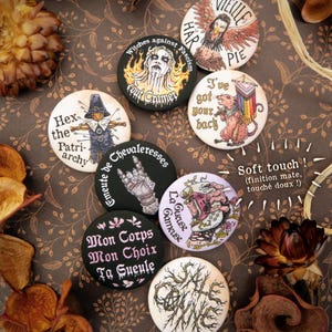 Op de afbeelding: Een verzameling ronde, kleurrijke buttons met diverse ontwerpen en tekst. De buttons tonen illustraties van een vogel, een hand en andere afbeeldingen. Teksten bevatten zinnen als "Witches against Fascism" en "I've got your back". De buttons hebben een soft-touch afwerking.