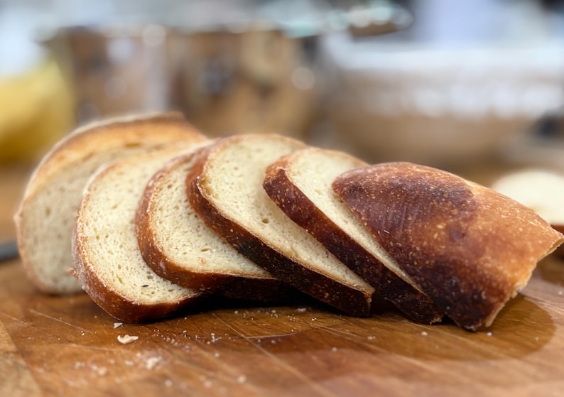 Puede incluir: Rebanadas de pan con corteza dorada y un interior claro, sobre una tabla de cortar de madera. Las rebanadas de pan est&aacute;n dispuestas para mostrar la textura y el color de los productos horneados.