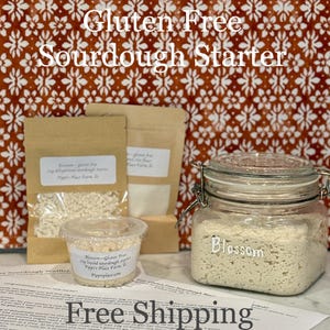 May include: A gluten-free sourdough starter kit with a glass jar labeled "Blossom", small bags, and a clear container. The text "Gluten Free Sourdough Starter" is at the top. The background is a patterned orange and white fabric.