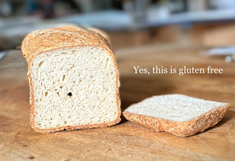 Puede incluir: Una hogaza de pan de color claro con corteza dorada, cortada para revelar una textura interior porosa. Junto a la hogaza hay una rebanada individual. El texto "Yes, this is gluten free" est&aacute; impreso en blanco a la derecha.