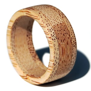 May include: A light brown bamboo ring with a patterned design. The ring is made from natural bamboo and has a smooth, polished finish.