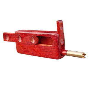 May include: A handcrafted wooden tool with a rich, reddish-brown finish. The tool features a rectangular body with a cylindrical wooden piece and a metal tip. The design includes a handle and a pointed end, suggesting a specialized function.