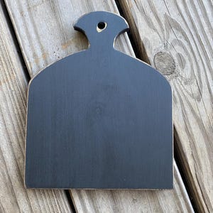 May include: Black wooden chopping board with a handle. The board has a distressed finish and is shaped like a teardrop.
