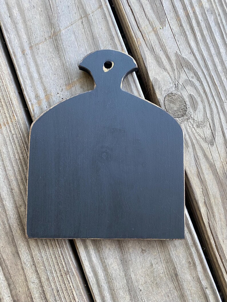 May include: Black wooden chopping board with a handle. The board has a distressed finish and is shaped like a teardrop.