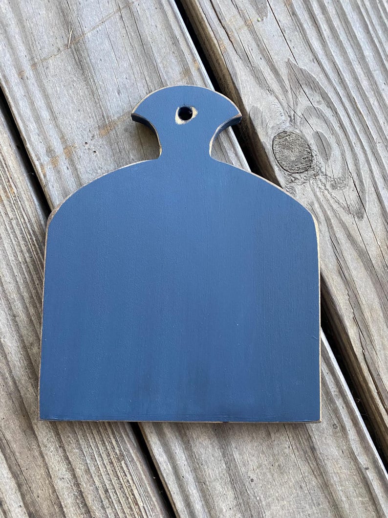 May include: A small, dark blue, wooden chopping board with a rounded top and a hole in the handle. The board is sitting on a wooden surface.