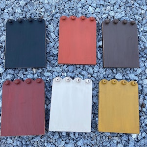 May include: Six wooden signs with scalloped edges and black knobs. The signs are painted in various colors, including black, red, white, brown, and yellow.