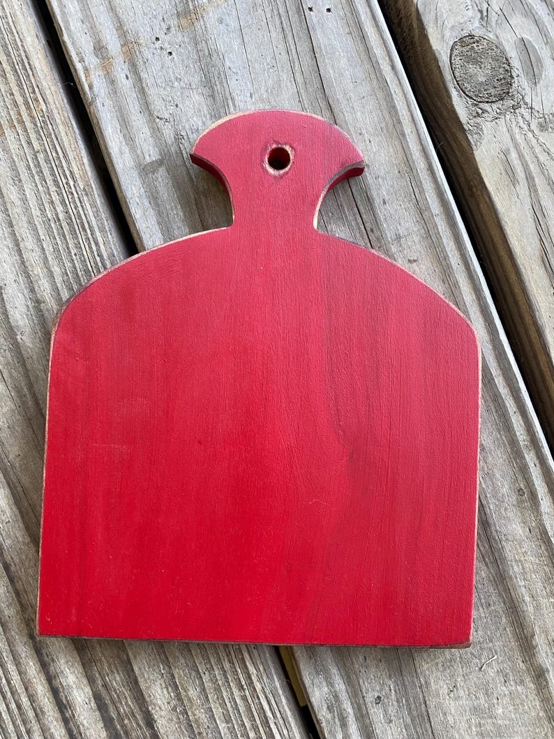 May include: A red wooden chopping board with a handle. The board has a rounded shape and a hole in the handle.