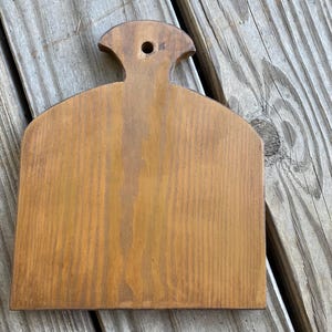 May include: A wooden kitchen utensil with a handle and a flat surface. The utensil is brown and has a natural wood finish.