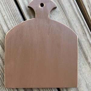 May include: A brown wooden chopping board with a handle. The board has a slightly rounded shape and a smooth surface.