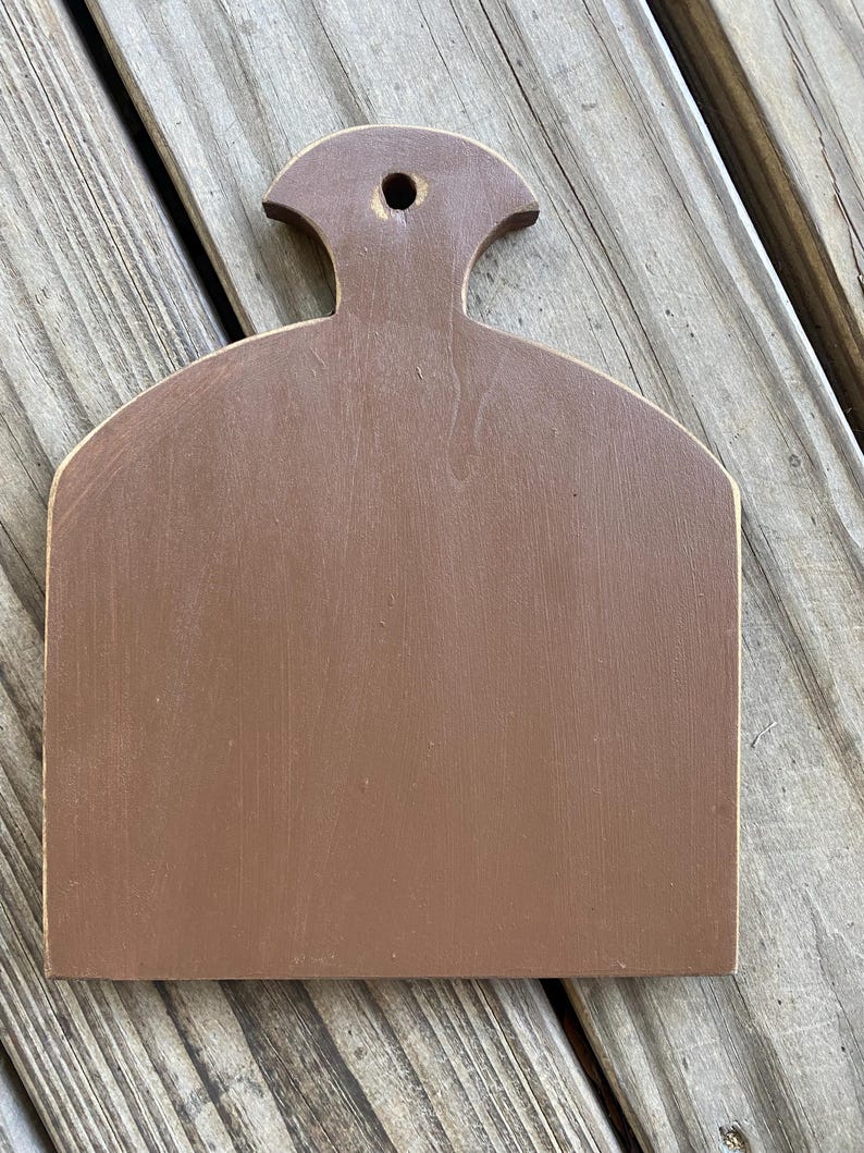 May include: A brown wooden chopping board with a handle. The board has a slightly rounded shape and a smooth surface.