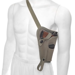May include: A light olive green shoulder holster with a strap, designed to be worn across the chest. The holster features a pocket for a handgun and an additional pocket. The handgun has a brown grip.