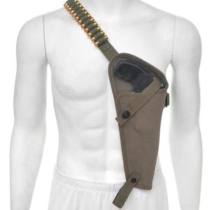 May include: Olive green shoulder holster with a black handgun. The holster has a strap with a row of gold-colored bullets. The holster is designed to be worn across the chest.