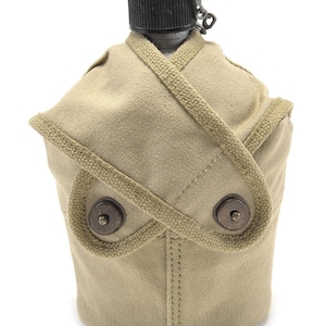 May include: A tan canvas canteen cover with two metal buttons and a brown leather strap. The cover is designed to fit a metal canteen.