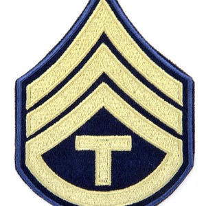 May include: A yellow and blue military rank patch with three chevrons and a 'T' in the center.