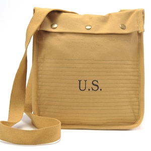 May include: A tan canvas messenger bag with a long adjustable strap. The bag has a flap with two metal snaps and the text "U.S." embroidered on the front.