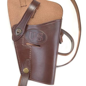 May include: A brown leather holster with a shoulder strap and a US marking. The holster has a flap and a snap closure.
