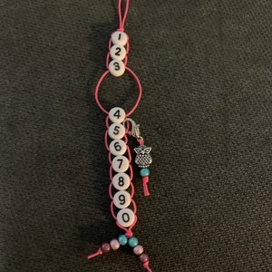 May include: Pink string with white beads numbered 1 through 10, a silver owl charm, and turquoise and purple beads.