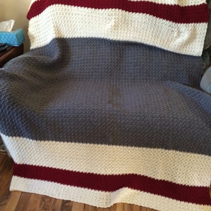 May include: A crocheted throw blanket with stripes of white, grey, and burgundy.