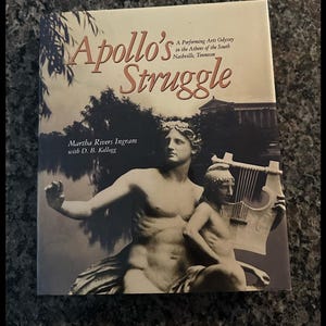 May include: A hardcover book titled Apollo's Struggle: A Performing Arts Odyssey in the Athens of the South Nashville, Tennessee by Martha Rivers Ingram with D. B. Kellogg, featuring a sepia-toned image of a classical statue with a lyre.
