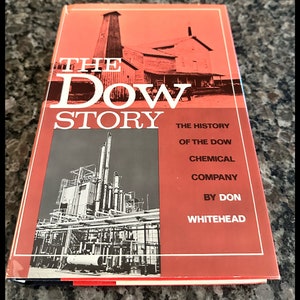 May include: A red hardcover book titled "The Dow Story: The History of the Dow Chemical Company by Don Whitehead". The cover features a black and white photo of an industrial plant.