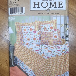 May include: A Simplicity Home 9149 sewing pattern envelope for bedding accessories. The cover features a bed with a white floral print comforter, orange and white plaid accents, and a matching bed skirt, all displayed in a bedroom setting.