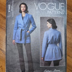 May include: Vogue Patterns sewing pattern V1663. The pattern features a woman wearing a light blue coat with a belt and pockets. The pattern also shows a back view of the coat. The text on the pattern reads "Vogue Patterns" and "Kathryn Brenne."