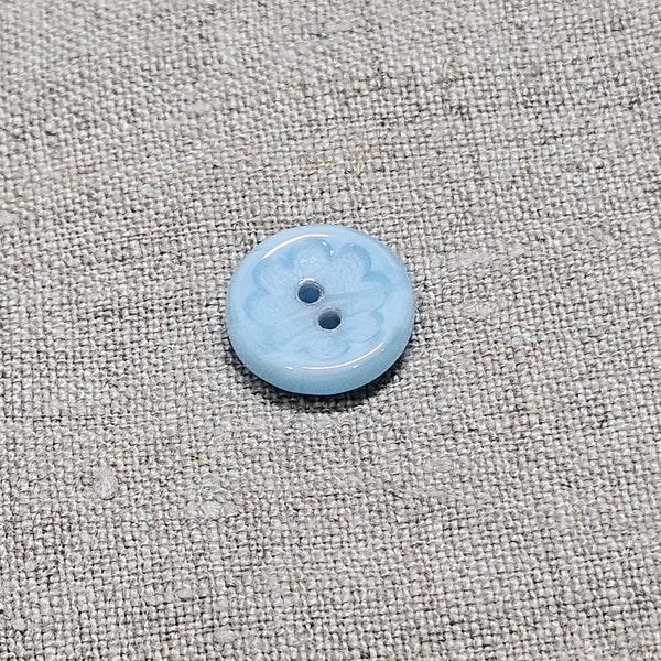 Vintage glass button. Round, pale blue, flower outline, sew through, 1/2"(1.3cm)  by 1/8th"