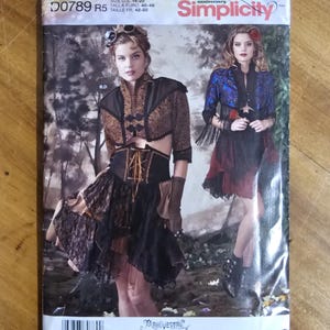 May include: A Simplicity sewing pattern envelope D0789 R5 for sizes 14-22. The front displays two outfits: a brown and black cropped jacket with a corset-style bodice and layered skirt, and a blue and black jacket with a dark skirt and fringe.