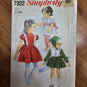 May include: Vintage Simplicity sewing pattern for a child's dress, size 5, with a breast measurement of 61 cm. The cover features illustrations of three different dress designs in red, white, and green.