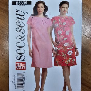May include: A See & Sew pattern envelope B5339 featuring two dress variations. The left dress is solid pink with a boat neckline and button details. The right dress features a floral print in shades of pink, red, and white. Text includes B5339 and Yes! It's easy.
