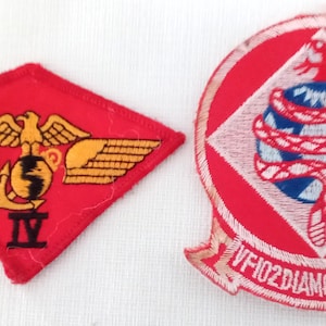 May include: Two embroidered patches. One is a red diamond with a gold eagle, wings, and anchor. The other is a red circle with a white diamond, a blue globe, and a red snake. Text reads "VF102DIAMONDBACKS".