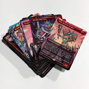 May include: A fan of collectible trading cards featuring fantasy characters and text. The cards have colorful illustrations and text, including "Krenko, Mob Boss" and "Zada, Hedron Grinder." The cards are from the "Secret Lair Drop" series.