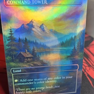 May include: A holographic "Command Tower" card featuring a scenic landscape with mountains, a lake, and a cabin. The card includes the text "Land" and a quote: "There are no wrong lands, just happy little colors."