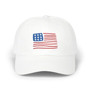 May include: A white baseball cap featuring an embroidered graphic on the front. The design consists of a blue rectangular field containing nine white stars, positioned to the left of several horizontal red lines representing a stylized flag.