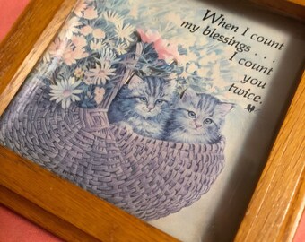 May include: A framed print with a quote that reads "When I count my blessings, I count you twice." The print features two kittens in a basket with flowers. The frame is made of wood and has a light brown finish.