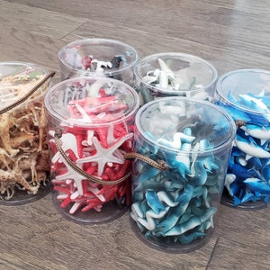 May include: Six clear plastic containers filled with various colorful plastic animal figurines. The containers are arranged in a semi-circle on a wooden surface. The figurines include giraffes, starfish, and sharks.