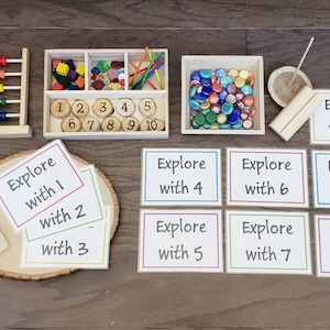Puede incluir: Un conjunto de materiales de aprendizaje Montessori para contar y explorar los n&uacute;meros. El conjunto incluye un &aacute;baco de madera, una bandeja con fichas de n&uacute;meros, una bandeja con gemas de vidrio de colores, una tabla de clavijas de madera y tarjetas con las palabras "Explorar con" y los n&uacute;meros del 1 al 10.