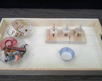 May include: A wooden tray containing a selection of items, including wooden blocks with the letters "t", "u", and "b" on them, a small bowl with wooden blocks spelling "Y", "Z", and "E", a small bowl with a red net and other small objects, and a small metal bowl.