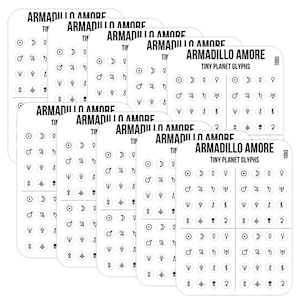 May include: A stack of white sticker sheets labeled Armadillo Amore Tiny Planet Glyphs. Each sheet features a grid of small black circular icons representing various planetary and astrological symbols arranged in neat rows and columns.