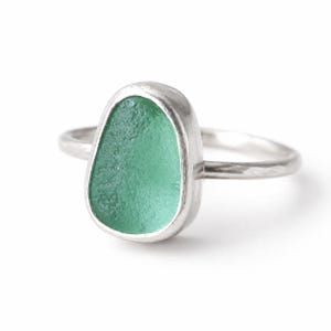 May include: A silver ring with a seafoam green, teardrop-shaped stone. The stone is set in a smooth bezel, and the band has a hammered texture. The ring is shown against a white backdrop.