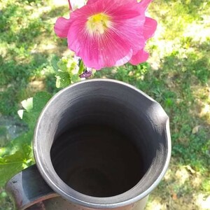 May include: A black ceramic pitcher with a wide opening and a handle. The pitcher is empty and has a smooth, glossy finish.