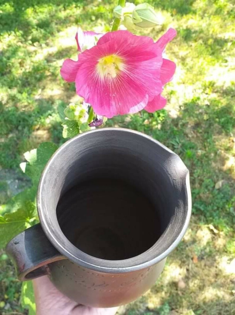 May include: A black ceramic pitcher with a wide opening and a handle. The pitcher is empty and has a smooth, glossy finish.