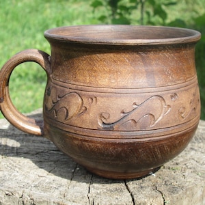 May include: A brown ceramic mug with a handle and a decorative design of stylised leaves and swirls.