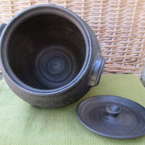 May include: A black ceramic pot with a lid. The pot has a wide opening and a round body. The lid has a small knob on top.