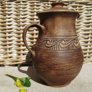 May include: A brown ceramic pitcher with a decorative design of swirling waves. The pitcher has a wide mouth and a handle.