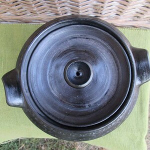 May include: Black ceramic pot with a lid and two handles. The pot has a smooth, glossy finish and a small hole in the center of the lid.