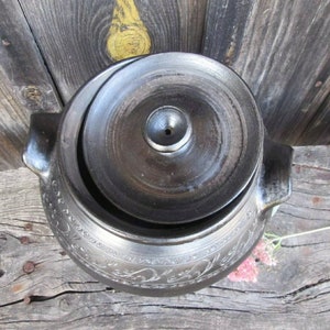 May include: A black ceramic pot with a lid, featuring an intricate floral design. The pot has a small hole in the lid.
