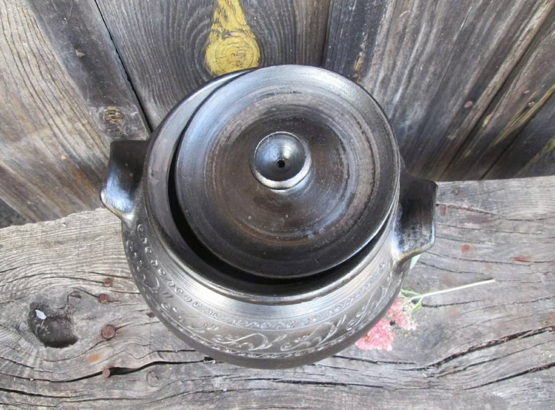 May include: A black ceramic pot with a lid, featuring an intricate floral design. The pot has a small hole in the lid.