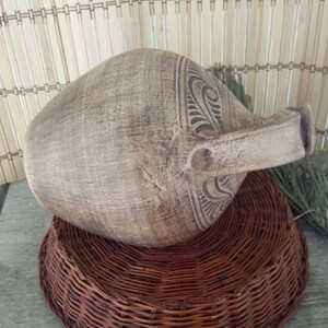 May include: A large, brown, ceramic pitcher with a carved design. The pitcher is sitting on a woven wicker base.