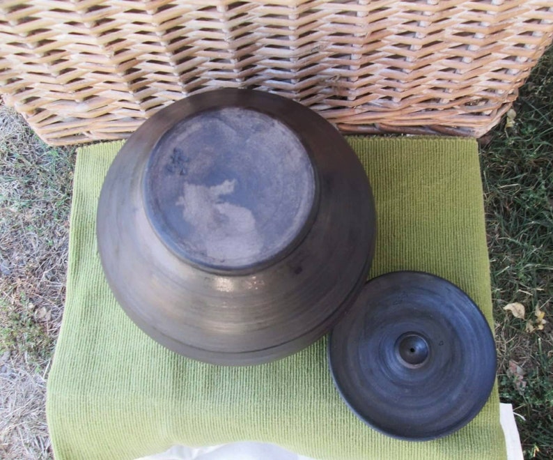 May include: A black ceramic pot with a lid. The pot is round and has a smooth surface. The lid has a small hole in the center.